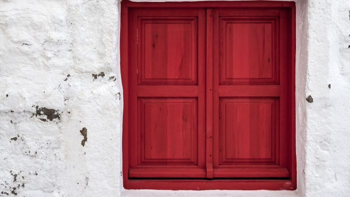 Volets en bois rouges avec une peinture semi-transparente, contrastant avec les murs blancs en chaux, sur une façade extérieure